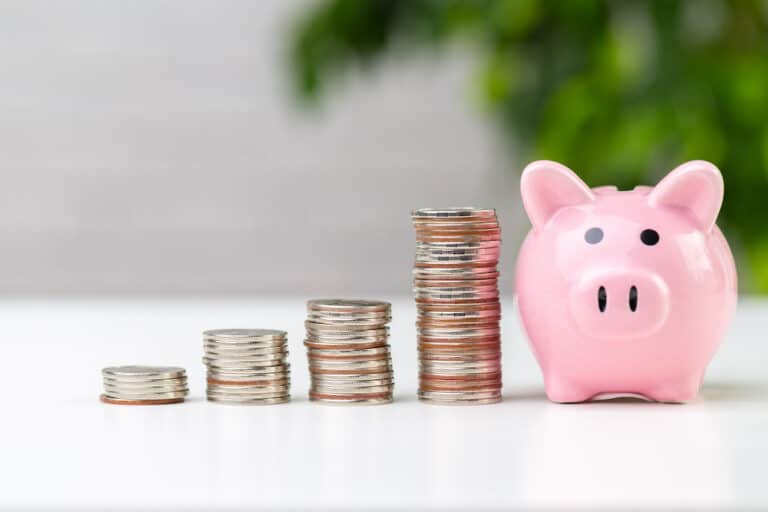 A piggy bank next to three stacks of coins on a table, representing reserve funding methods.